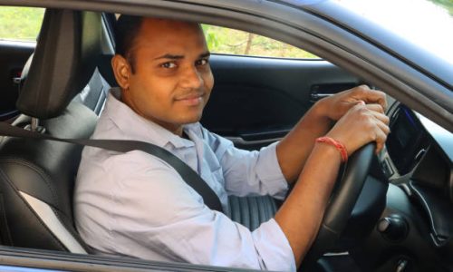 Stock photo showing an Indian man driving in his car (a private hire taxi cab car), wearing a seatbelt and looking out of open driver's window.